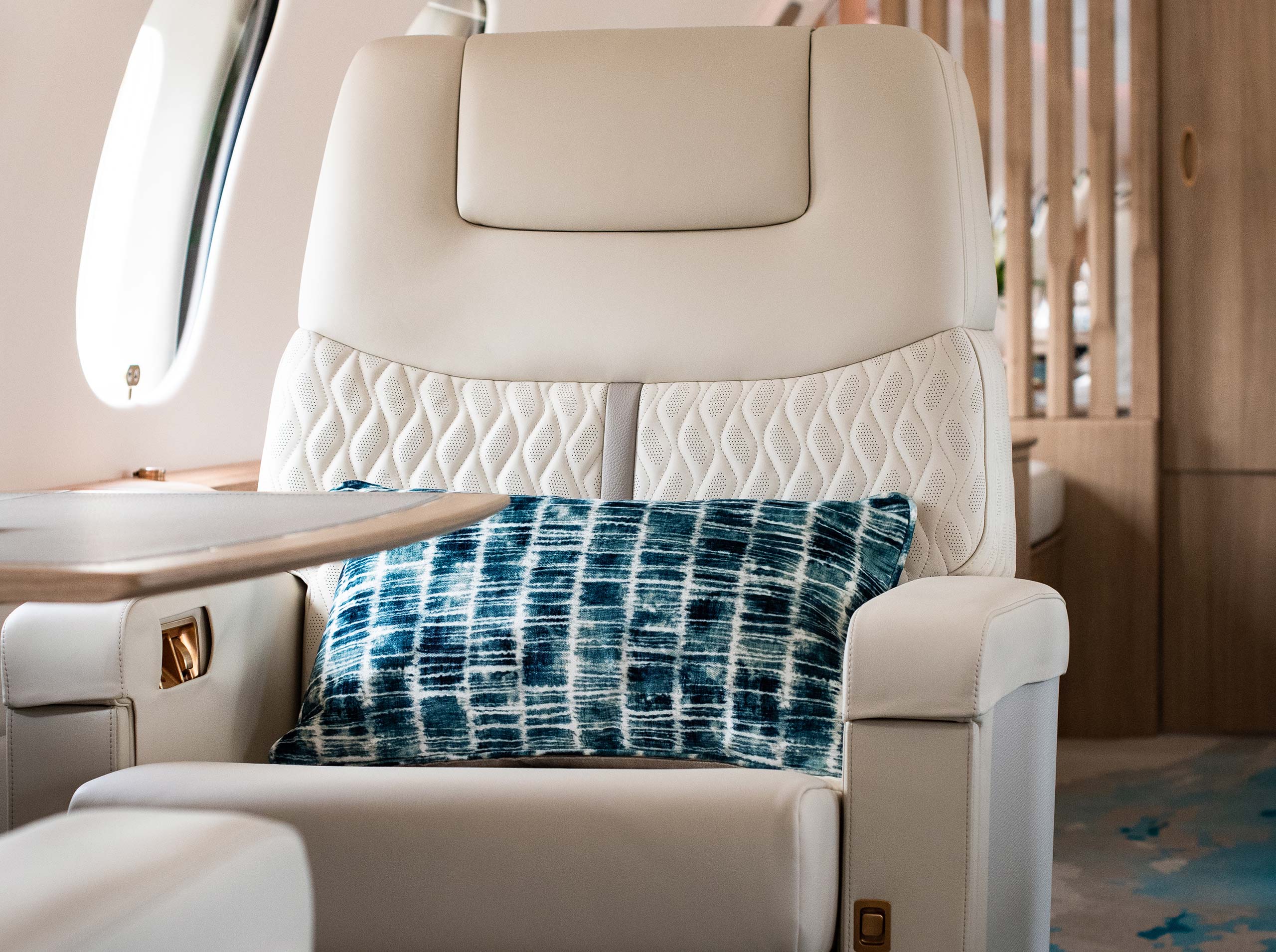 Nahaufnahme eines Global 6000 Sitzes mit blauer Zierkissen, perforierter Ledersteppung und Fensterblick