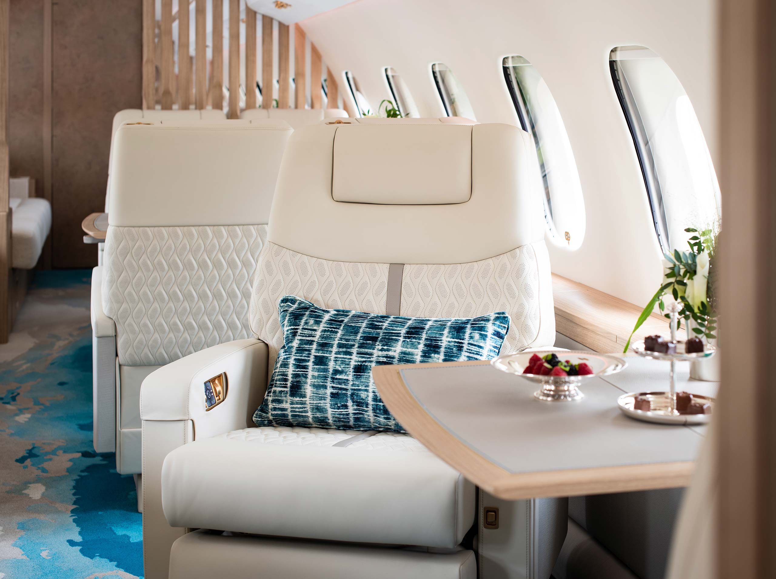Luxuriöser Einzelsitz mit blauer Zierkissen und ausklappbarem Tisch mit Pralinenarrangement in der Kabine einer Global 6000