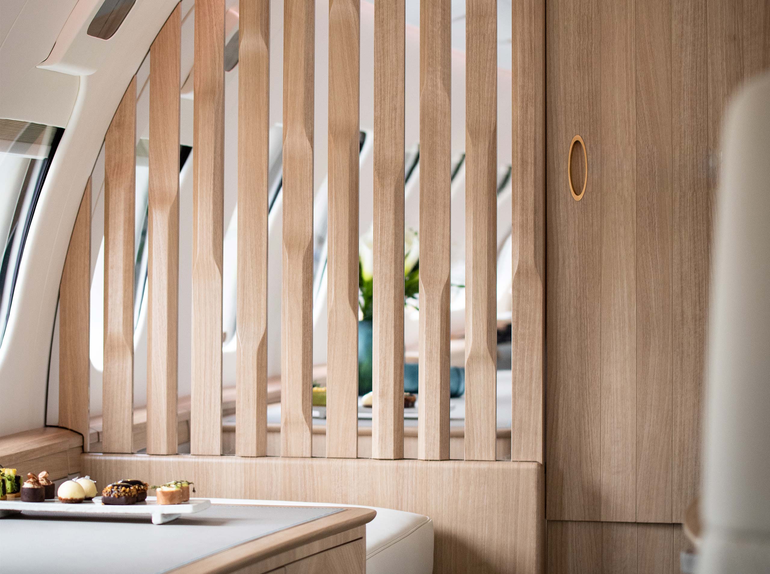 Detailansicht einer Kabinentrennwand aus hellem Holz mit vertikalen Lamellen in einer Global 6000, davor ein Sideboard mit edler Patisserie