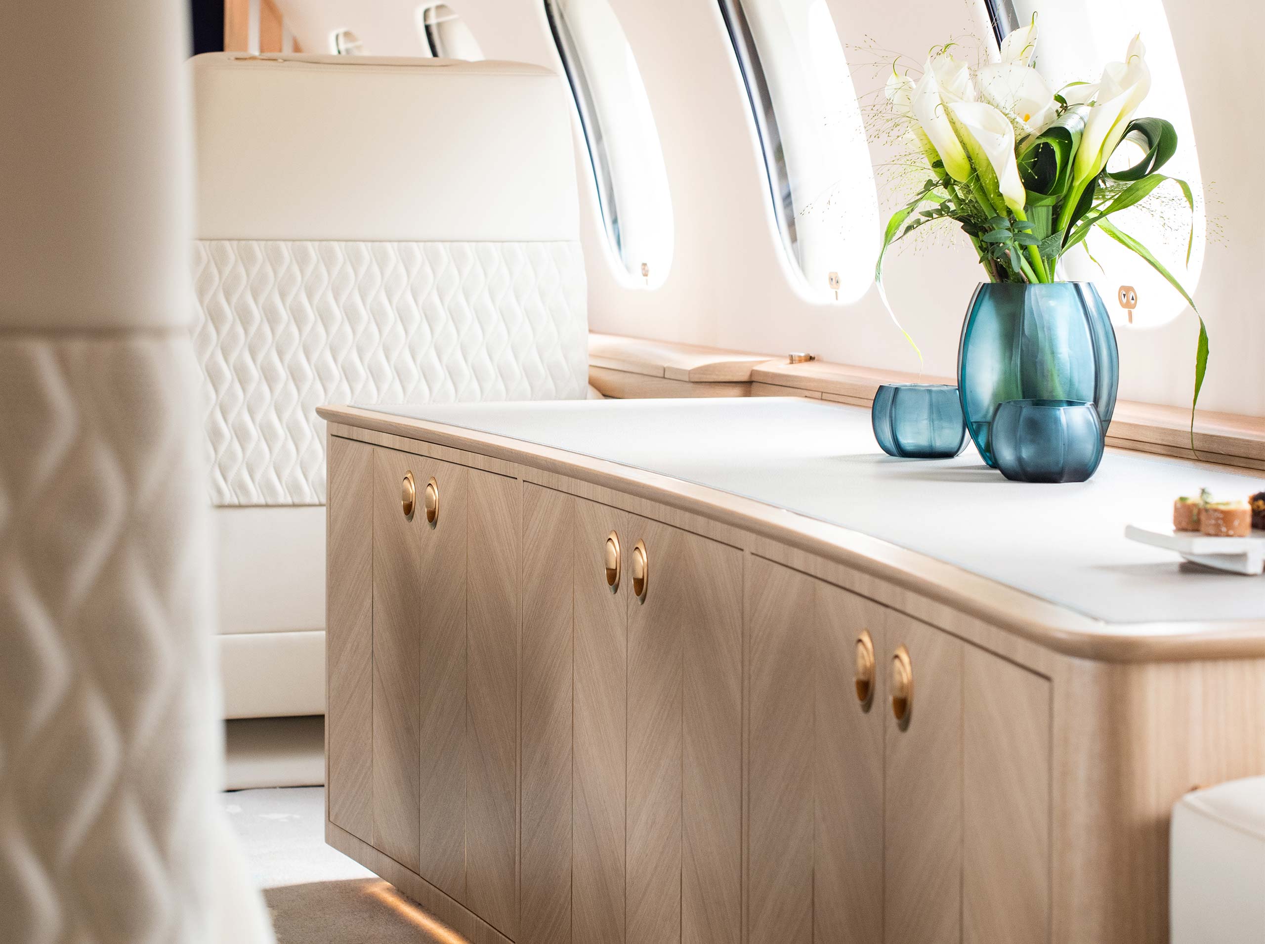 Detailansicht eines Sideboards mit hellem Holzfurnier, goldenen Griffen und blauen Vasen mit Calla-Blumen
