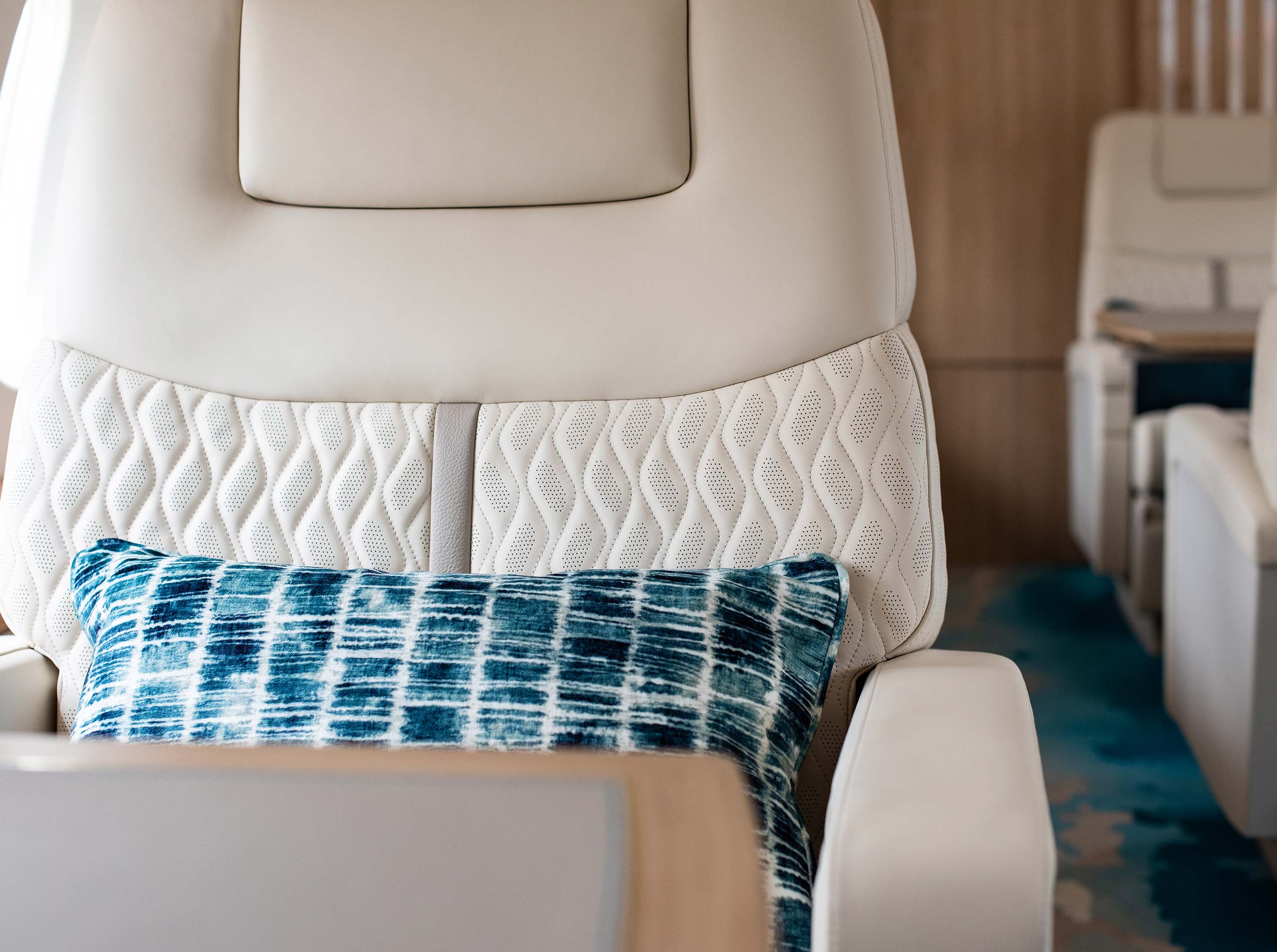 Detailaufnahme eines Kabinensitzes in einer Global 6000 mit heller Lederpolsterung, Ziersteppung und blauem Dekokissen