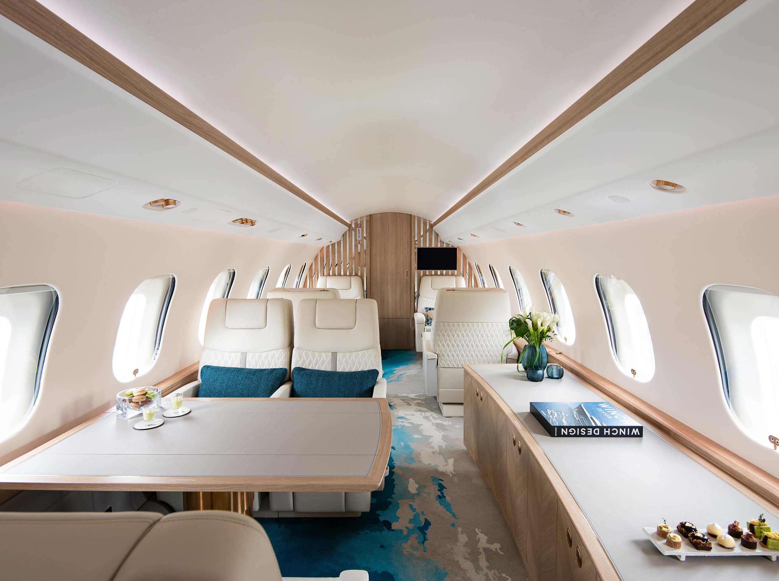 Breitwinkelaufnahme der Global 6000 Kabine mit Doppelsitzen, ausklappbaren Tischen, Sideboard und Sicht auf das Trennwanddesign