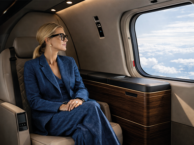 Une femme est assise dans l'habitacle raffiné d'un hélicoptère, aux finitions en bois, et regarde le ciel par le hublot