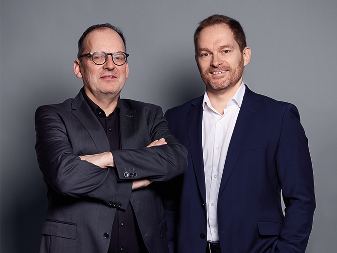 Thorsten Hirsch und Andreas Aigner stehen gemeinsam vor grauem Hintergrund. Die Aufnahme zeigt die Integration von HIRSCH Interieur in die F/LIST Gruppe zur Stärkung der Engineering-Kompetenzen von F/YACHTING.