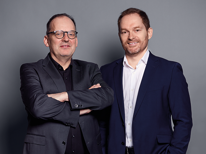 Thorsten Hirsch und Andreas Aigner stehen gemeinsam vor grauem Hintergrund. Die Aufnahme zeigt die Integration von HIRSCH Interieur in die F/LIST Gruppe zur Stärkung der Engineering-Kompetenzen von F/YACHTING.